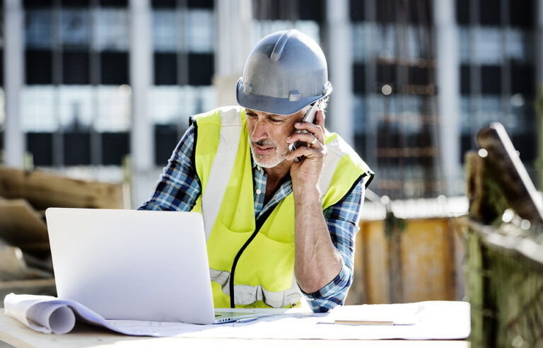 Male architect using mobile phone and laptop at construction site