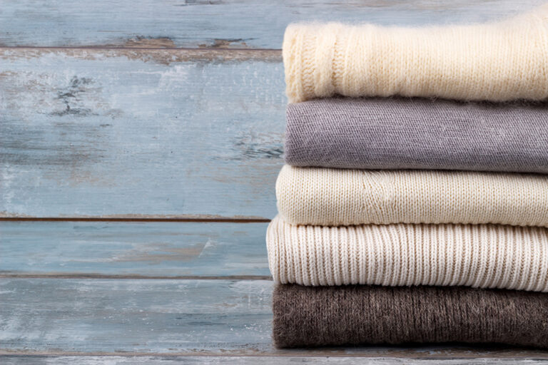 Stack of white and gray cozy knitted sweaters on rustic wooden background